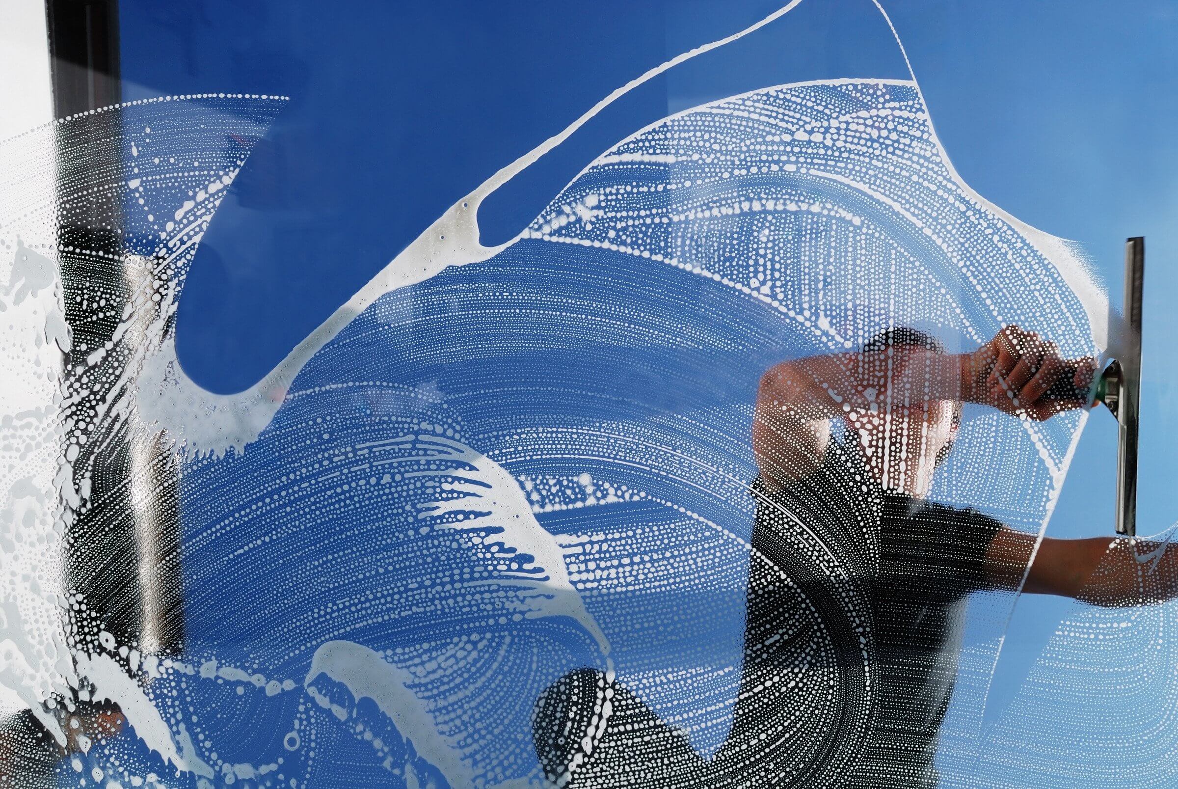 Rang Services technician squeegeeing a soapy storefront window against a blue Sacramento sky